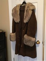 Front view of brown velour lambskin coat with shearling collar and cuffs hanging on hanger