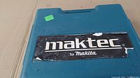 Blue molded plastic case lid with large "maktec by Makita" logo on black and white sticker, showing wear.