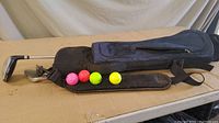 Four child's golf clubs (driver, 5 iron, 9 iron, putter) laid flat on cardboard surface next to four golf balls and a black carrying bag.