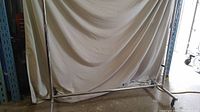 Chrome tubular clothes rack with wheels. Wide base and horizontal hanging bar visible. Positioned against a beige backdrop.