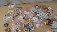 Wide view of various costume jewellery items in multiple plastic bags and loose, showing different jewelry pieces on a brown surface.