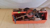 Photo showing an orange box filled with various vintage hand drills with wooden handles and metal gears, some rust and dust visible.