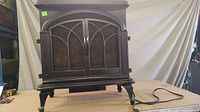 Front view of black Maskoka electric fireplace with closed decorative metal mesh doors and power cord visible.