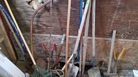 Photo showing various garden tools standing upright against a wooden wall, including shovels, rakes, cultivators, and a hoe.