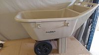 Side view of the beige Easy Roller Jr. gardening wagon showing the wheel and body design.
