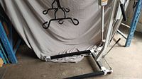 White Hoyer patient lift with arm extended and sling hanging, positioned on a warehouse floor with a grey backdrop.