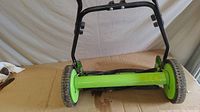 Front view showing green body, black handle, and wheels of manual push lawn mower