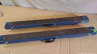 Two folded blue painted metal horses with black plastic handles, lying flat on a surface.