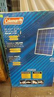 Box showing Coleman brand and product details: 100 watt 12 volt crystalline solar panel, weatherproof, shatterproof, waterproof, maintenance free.