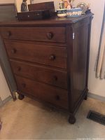 View of antique wooden dresser with four drawers and wooden knob handles, standing on bun feet, with visible marks and scratches.