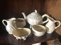 Front view showing teapot, two creamers, and three bowls/dishes on shelf