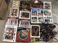 Multiple boxes of assorted glass ornaments plus string lights and village set laid out on floor