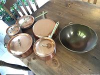 Overhead view of four copper pots with lids on a wooden table, showing polished copper exteriors and brass handles.