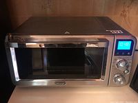 Full front view of the stainless steel Delonghi convection toaster oven on counter showing digital display and door