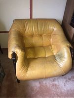 Front view of mustard yellow tufted leather seat showing wear and a small tear on left arm