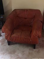 Front view of orange leather lounge chair with tufted seat and back showing overall shape and surface wear