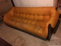 Front view of mustard leather sofa with tufted seat and back showing wear and tears on right side