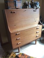 Angled front view of desk showing drop-down writing surface closed, wooden veneer finish and recessed handles