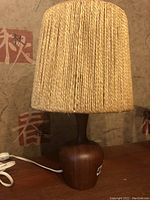 Full view of the lamp showing the teak wood base and rope shade, photographed from a side angle.