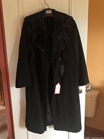 Full view of long black coat with dark mink fur collar hanging on door.