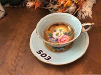 Top view of Paragon teacup placed on saucer showing blue rim, gold inner circle, and floral center design.