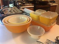 Photo shows four nested yellow and white Pyrex mixing bowls and four yellow Pyrex refrigerator dishes with lids, arranged on a kitchen counter.