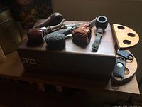 Overview of wooden humidor box with four smoking pipes on top, wooden pipe rack and cigar cutters beside it