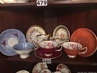 Full view of all five teacups and their matching saucers arranged on a wooden shelf.