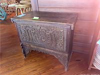 Full photo of the antique carved wood storage chest showing front panel and overall structure on wooden floor.