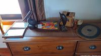 Photo of dresser top with multiple lot items: wood dolphin and pelican figurines, colorful Haitian painting, rattan tissue holder, small wooden box, and circular wood/wicker plaque.