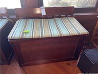Front angled view of wooden toy chest with closed striped cushion lid, showing wood finish and overall structure.
