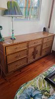 Front view of wood dresser with rattan and wicker drawers and decorative lamp on top.