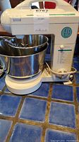 Front view of vintage Hamilton Beach ProMix 275 watt stand mixer with stainless steel bowl and wire whisk attachment on blue tiled surface.