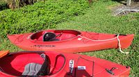 Side and top view of the red Heritage Feather Lite Pro kayak set on grass showing full length, cockpit, and deck details.