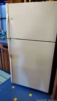 White Kenmore refrigerator full view showing top freezer and main compartment, standing on blue floor mat near kitchen cabinets.