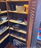 Cabinet shelves with various bowls, colander, flatware, and roasting pan box