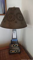 Full view of lamp showing punch tin shade with circular punched designs and colored glass pieces, and square metal base with multi-colored tile inlays, approximately 28 inches tall.