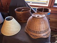 Four wicker and cane lamp shades of varying shapes and sizes on a couch surface near a window, showing full lot content.