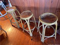 Three vintage rattan bar stools aligned in a row showing overall shape and size against wood paneling wall and hardwood floor.
