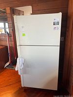Front view of the white Kenmore top-freezer refrigerator; exterior shows some scratches and a towel hanging on the handle.