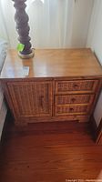 Side table showing top with smooth wood finish and three drawers plus one cabinet door with wicker panel.