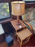 Two bamboo nesting tables with woven tops and bamboo frames placed adjacent to a turned wood table lamp with burlap lampshade. Shows natural bamboo textures and wear including scratches.