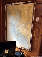 Front view of the large U.S. Coast Guard marine map framed in wood with rope border hung on wood-paneled wall. Shows map details and nautical features.