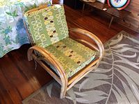 Full view of the vintage rattan chair with green patterned cloth cushions showing frame and cushions.