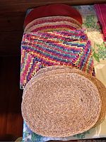 Photo showing multicolored woven rectangular placemats and a round natural woven placemat on top.
