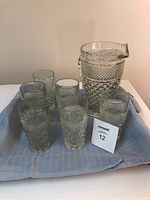 Photo showing 6 clear textured glass drinking glasses and 1 matching pitcher on a cloth.