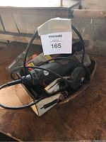 Electric angle grinder in black and grey with power cord resting in a cardboard box on a wooden surface.