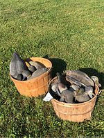 Two wooden baskets sitting on green grass filled with several plastic bird decoys with attached weights. Mostly visible are large decoys resembling geese or ducks.