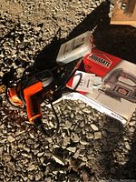 Jobmate jigsaw in box with Black & Decker drill and plastic case with bits on gravel surface.