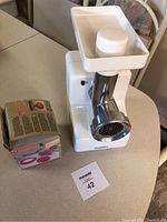 Electric Maxim brand meat grinder with white plastic body, metal grinding disc, and feeding tray on top shown on table.